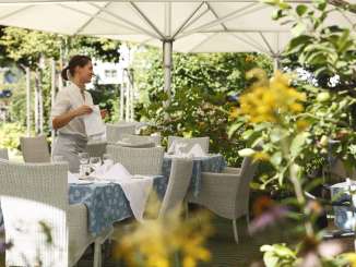 Gartenvilla Sommerlust Ein blühender Restaurantsgarten ist mit geflochtenen Tischen und Stühlen ausgestattet. Die Tische sind gedeckt.