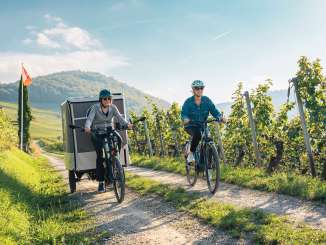 Zwei Freundinnen fahren durch die Reben. Eine mit dem E-Bike und eine auf dem Cargovelo mit einem aufklappbarem Zeltaufbau.