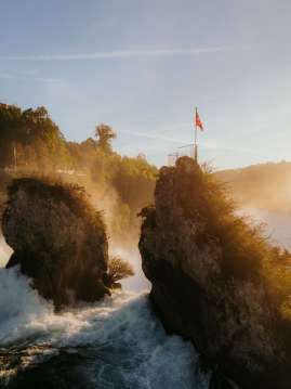 Rheinfall im Herbst Blick von hinten auf die zwei Felsen mitten im Wasserfall. Goldies Licht scheint auf den Wasserfall.