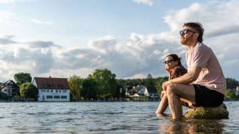 Zwei Personen sitzen auf grossen Steinen im Rhein und kühlen die Füsse im Wasser ab.