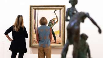 Zwei Frauen stehen vor einem Bild, auf dem ein Mann mit einer Axt einen Baum fällt.